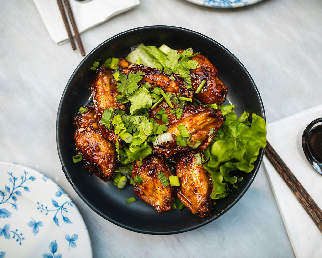 Chicken wings simmering in glossy soy sauce in a pan, surrounded by fresh vegetables such as carrots and spring onions, creating a warm and savoury home-cooked scene.