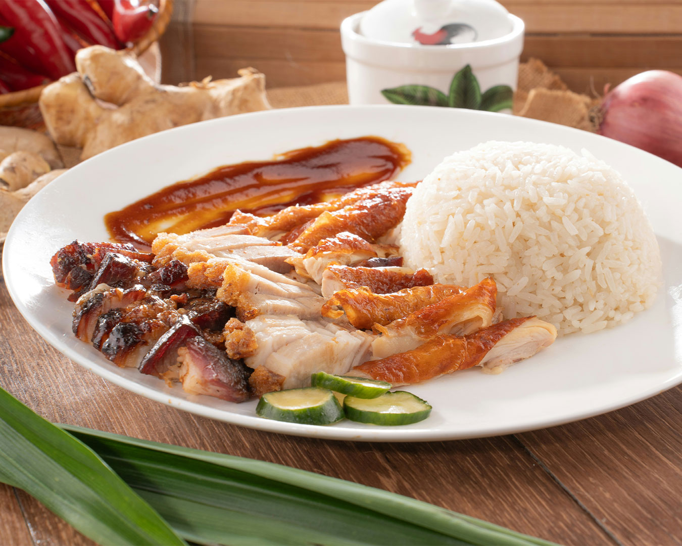 A plate of tender sliced chicken served over fragrant rice, accompanied by cucumber slices and dipping sauces, presented as a classic comfort meal.