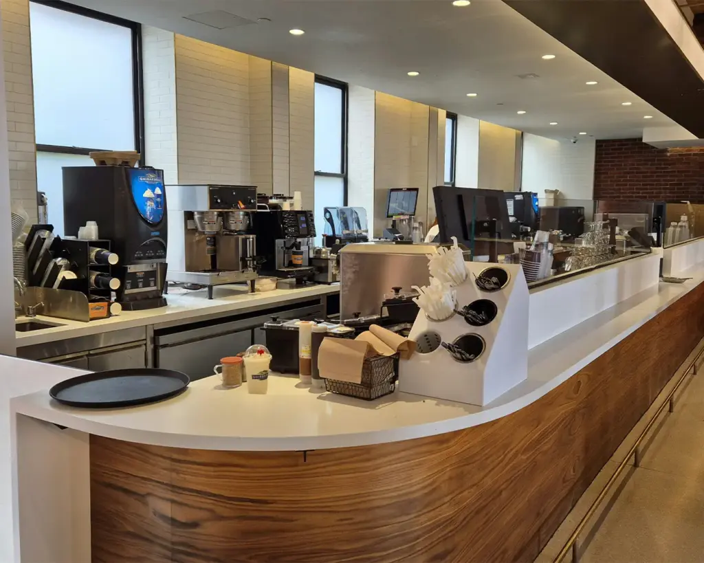 A café counter where a barista prepares freshly brewed coffee, with an espresso machine, cups, and coffee tools arranged neatly. The setting captures the warm, inviting atmosphere of a café as drinks are crafted for customers.