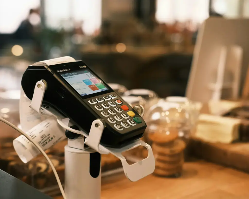 A card payment terminal placed on a café counter, ready for customers to tap or insert their cards. The device sits beside the cashier area, highlighting the convenience of modern contactless payments.