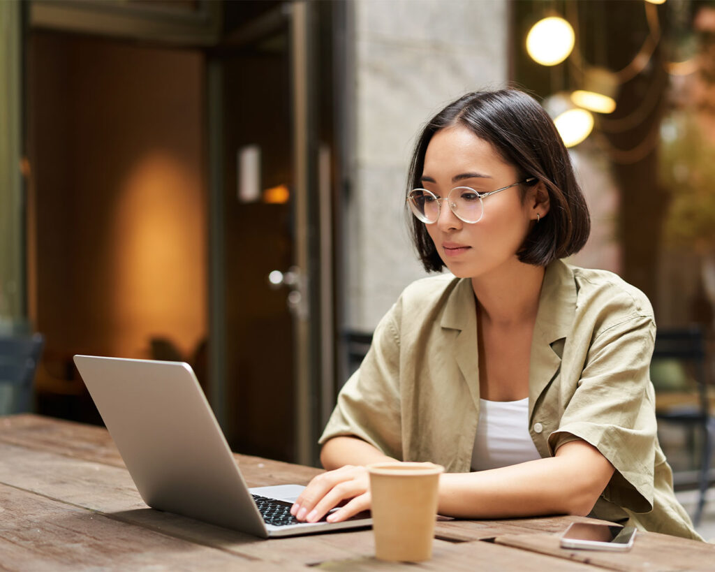 A woman sitting at a desk while working on her laptop, focused on the screen in a bright indoor workspace with a calm and productive atmosphere.