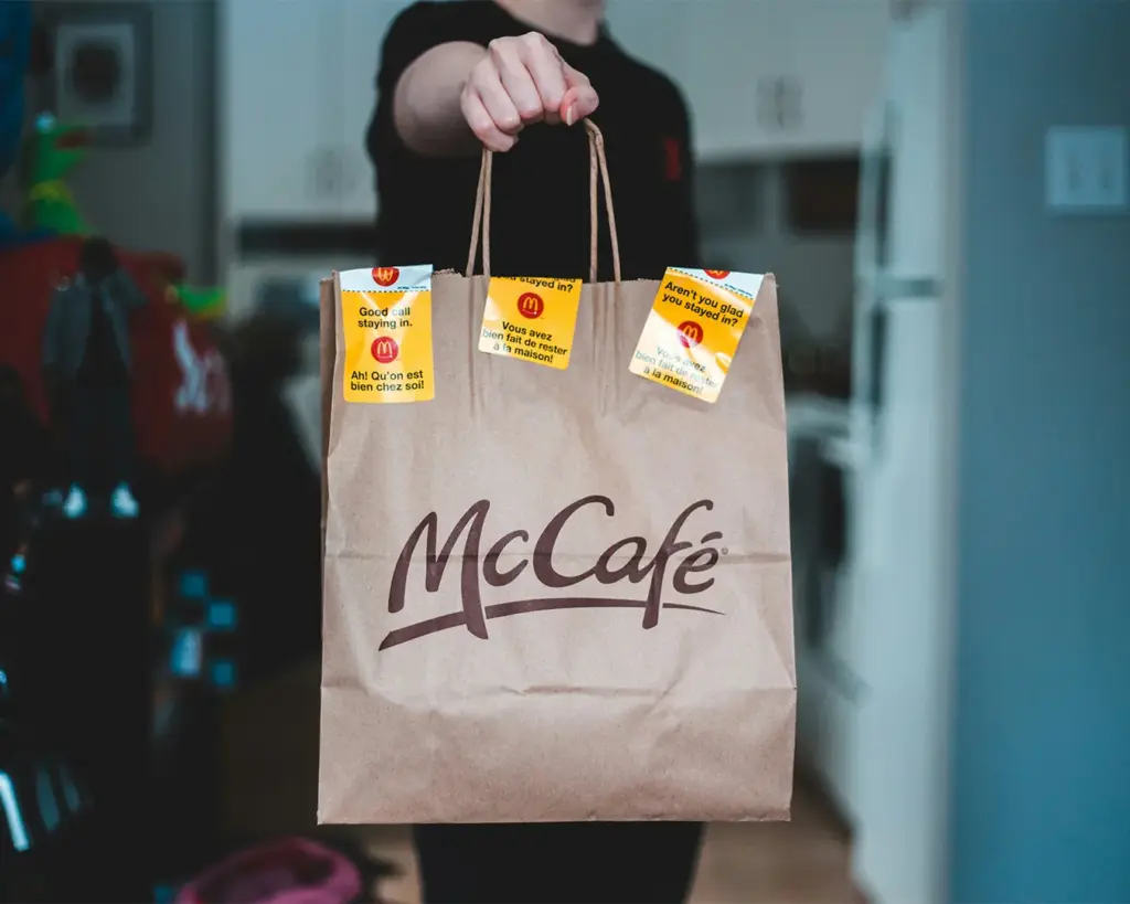 A hand holding a McDonald’s takeaway paper bag filled with fast-food meals, ready to be carried out of the restaurant.