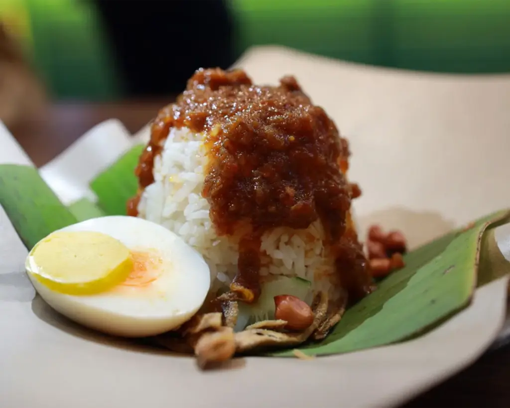 A small portion of nasi lemak neatly wrapped in banana leaf, containing coconut rice and sambal, a common takeaway style in Malaysian street food culture.