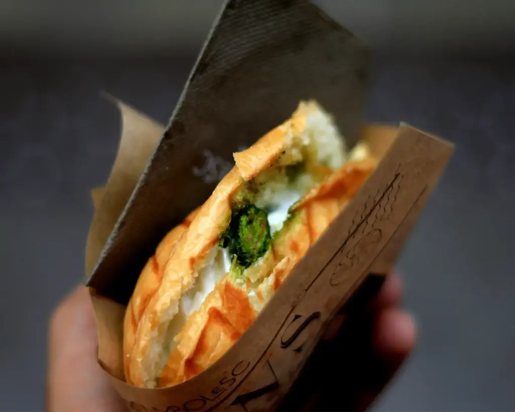 A hand gripping a fresh wrap filled with layers of vegetables, meat, and sauces, perfectly packed for a convenient and delicious street food bite.