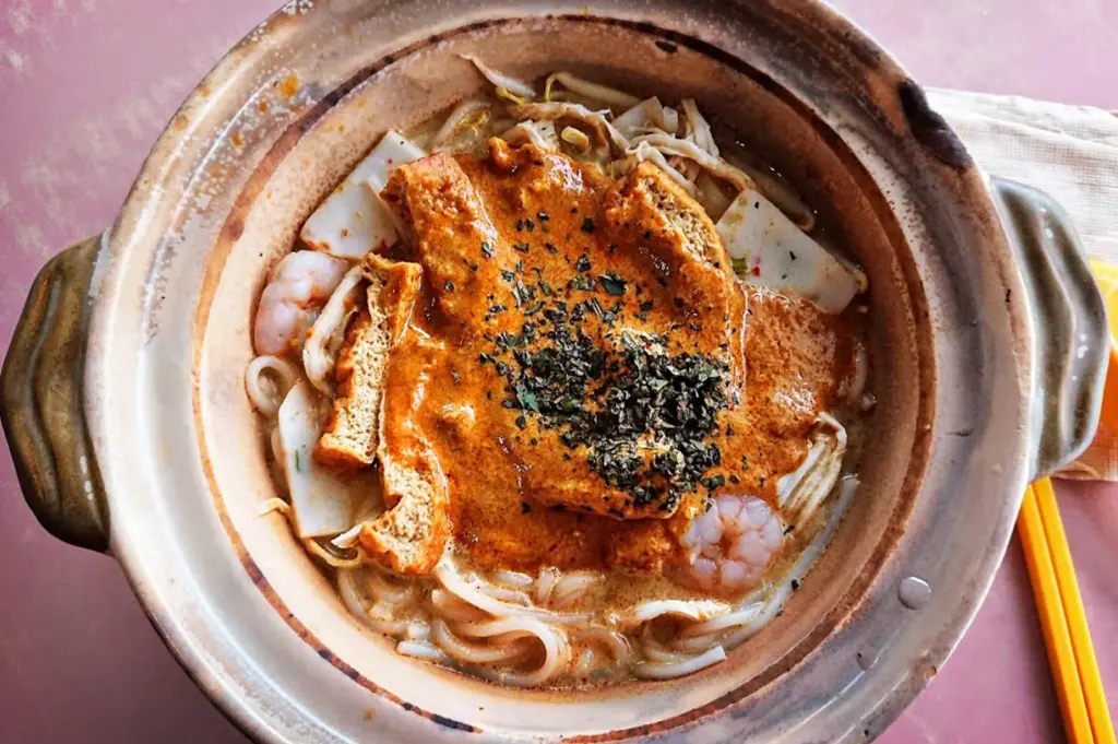 Authentic Singapore claypot laksa from Depot Road Zhen Shan Mei in Alexandra Village, Singapore, featuring a rich, bubbling curry gravy over thick noodles, prawns, and tau pok.