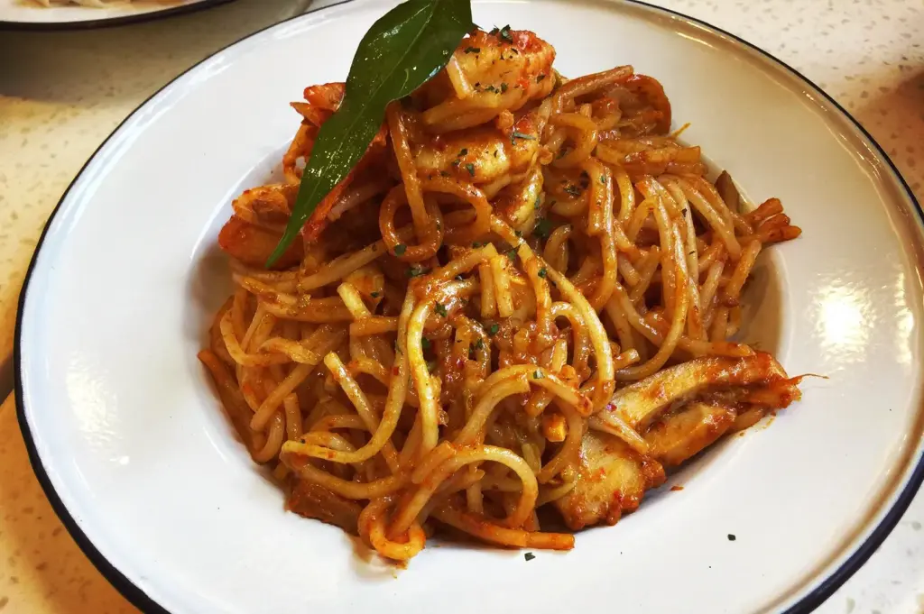 A modern dish of dry laksa noodles from Curry Times in Singapore, stir-fried in aromatic laksa paste and topped with prawns, fishcakes, and a fresh laksa leaf.