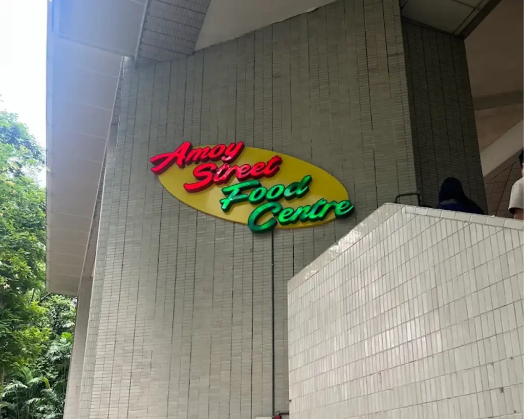 A prominent Amoy Street Food Centre signage displayed at the entrance, featuring bold lettering that welcomes visitors into one of Singapore’s well-known hawker centres, bustling with local food culture and everyday diners.