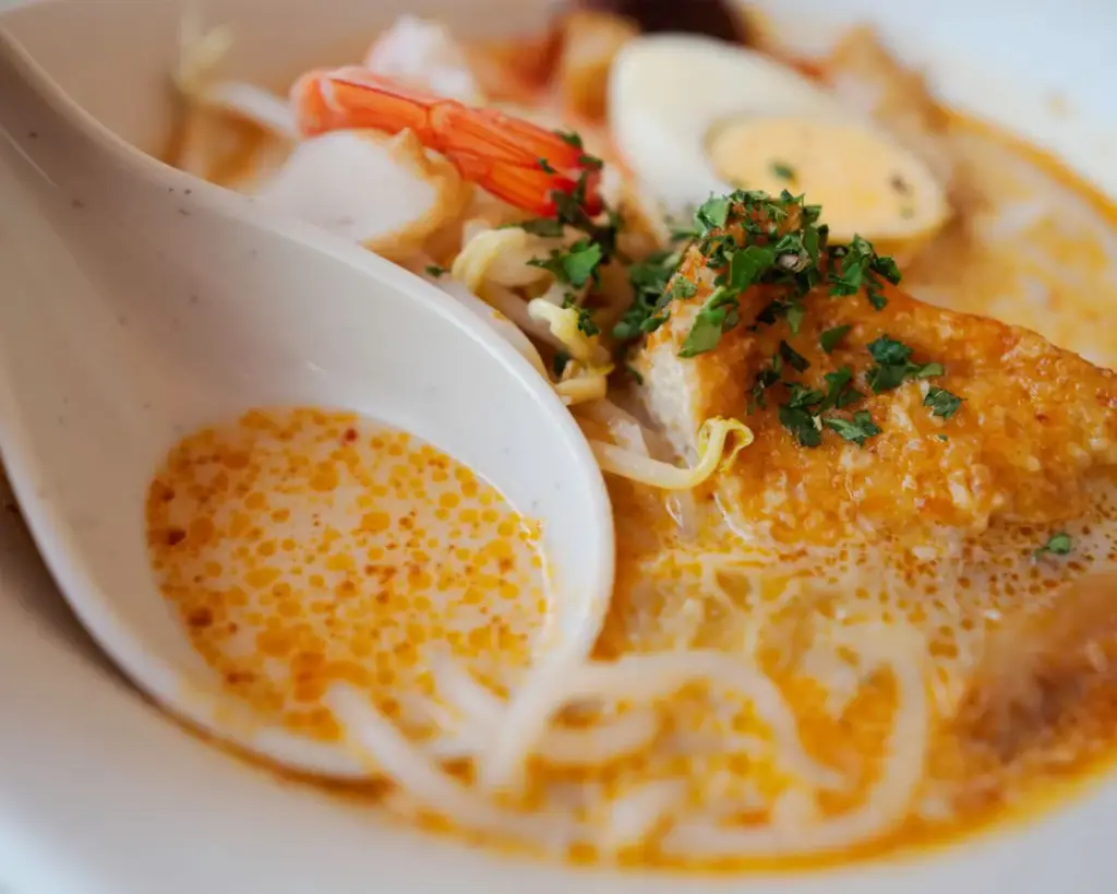 A bowl of spicy noodle soup featuring shrimp, sliced egg, and vegetables, garnished with herbs, creating a warm and appetizing presentation.