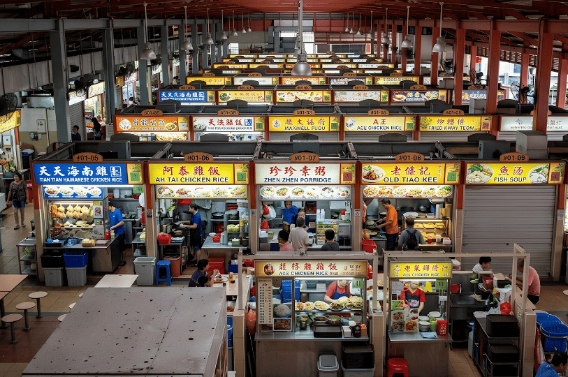 An overhead view of the bustling hawker stalls inside Maxwell Food Centre, highlighting colorful signboards for famous spots like Tian Tian Hainanese Chicken Rice and Zhen Zhen Porridge as patrons queue for food.