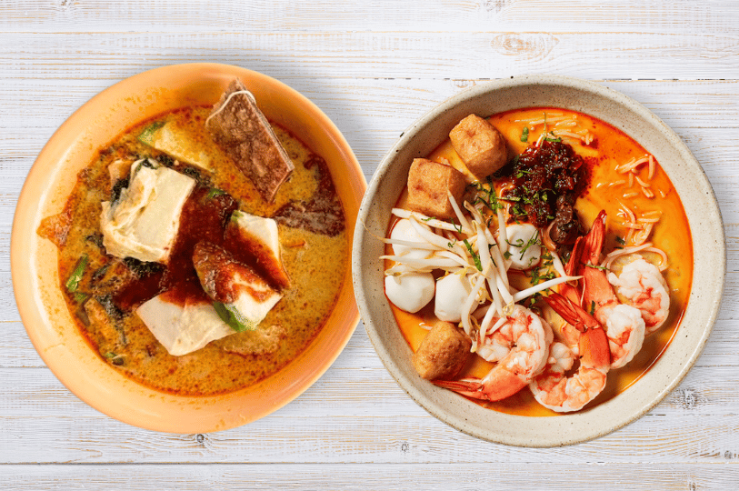 A top-down comparison of two distinct noodle soup bowls, with the bowl on the right prominently featuring a crucial, dark red dollop of sweet and fiery sambal chili resting on top of the ingredients, waiting to be stirred into the coconut broth.