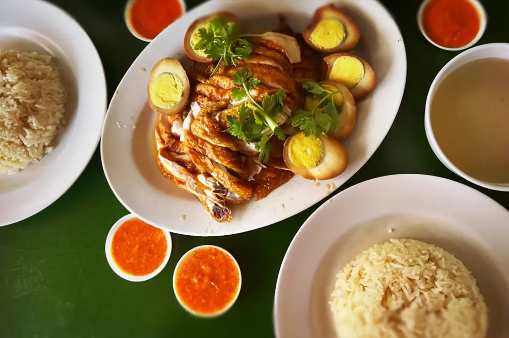 A platter of Seng Heng Hainanese Boneless chicken served with braised hard-boiled eggs, side bowls of seasoned rice, soup, and chili dipping sauce from Seng Heng at Geylang East Food Centre.